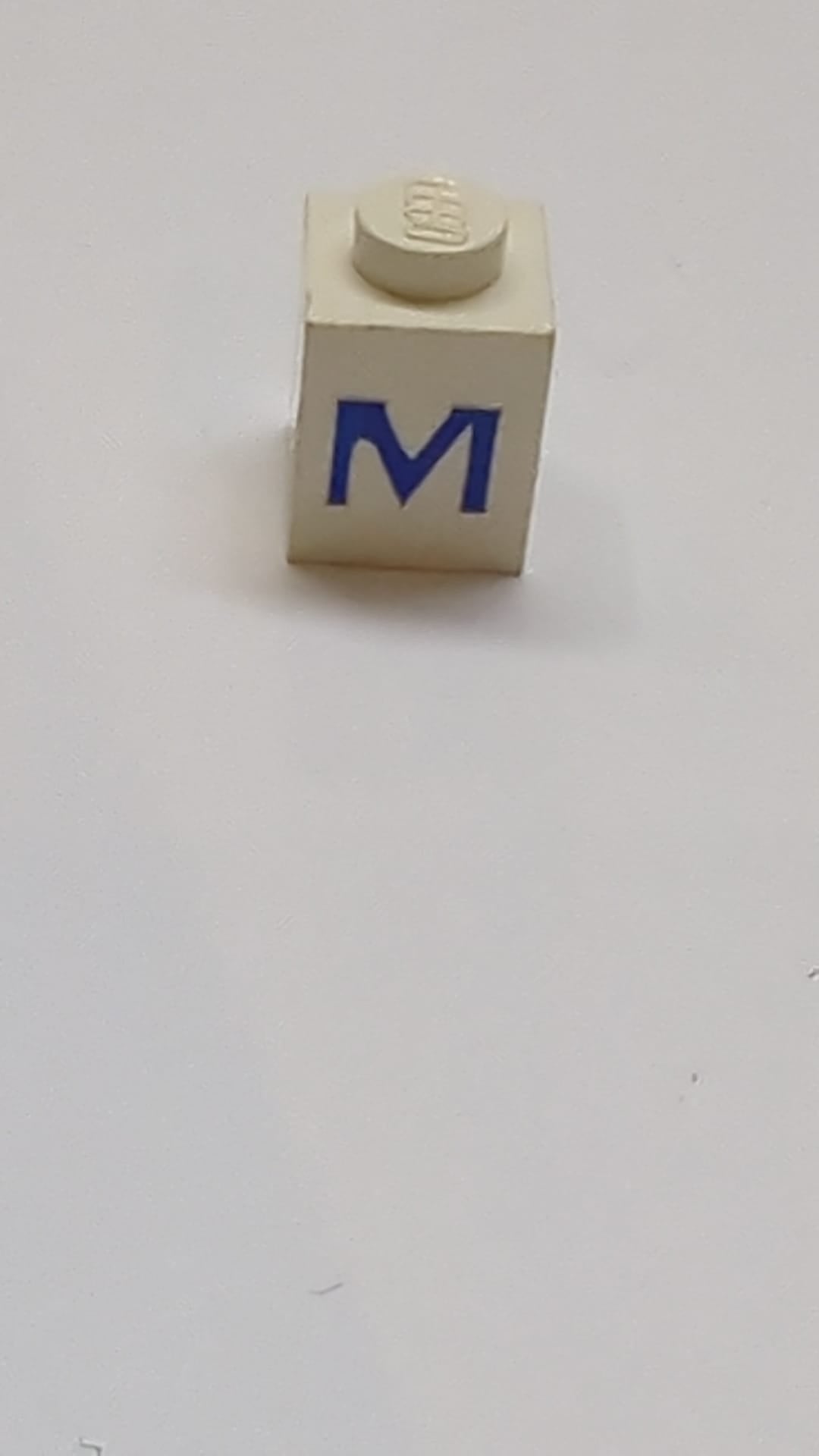 1x1 Stein mit blauem Großbuchstaben-M-Muster weiß