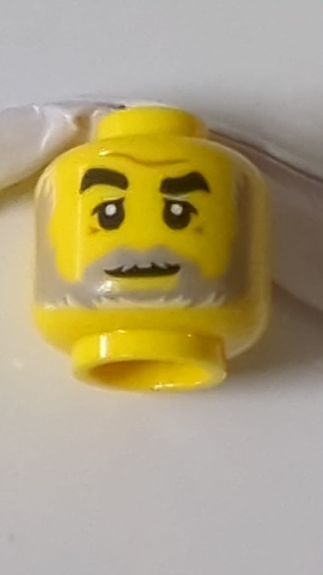 Minifigur, Kopf: Schwarze Augenbrauen, rechts hochgezogen, mittlere nougatfarbene Brauenfalte, Krähenfüße, hellblaugrauer Bart mit weißen Highlights, leichtes Grinsen gelb