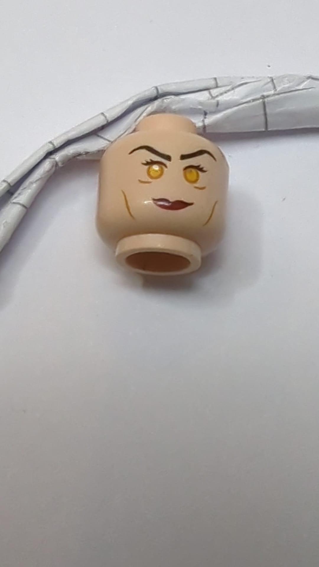 Minifigur, doppelseitiger Kopf, weiblich, schwarze lange Augenbrauen, Wimpern, mittelbraune Wangenfalten, rote Lippen, verschmitztes Lächeln, Grübchen am Kinn und silberne Schutzbrille / neutrales orangefarbenes Augenmuster hellnougat (fleischfarben)