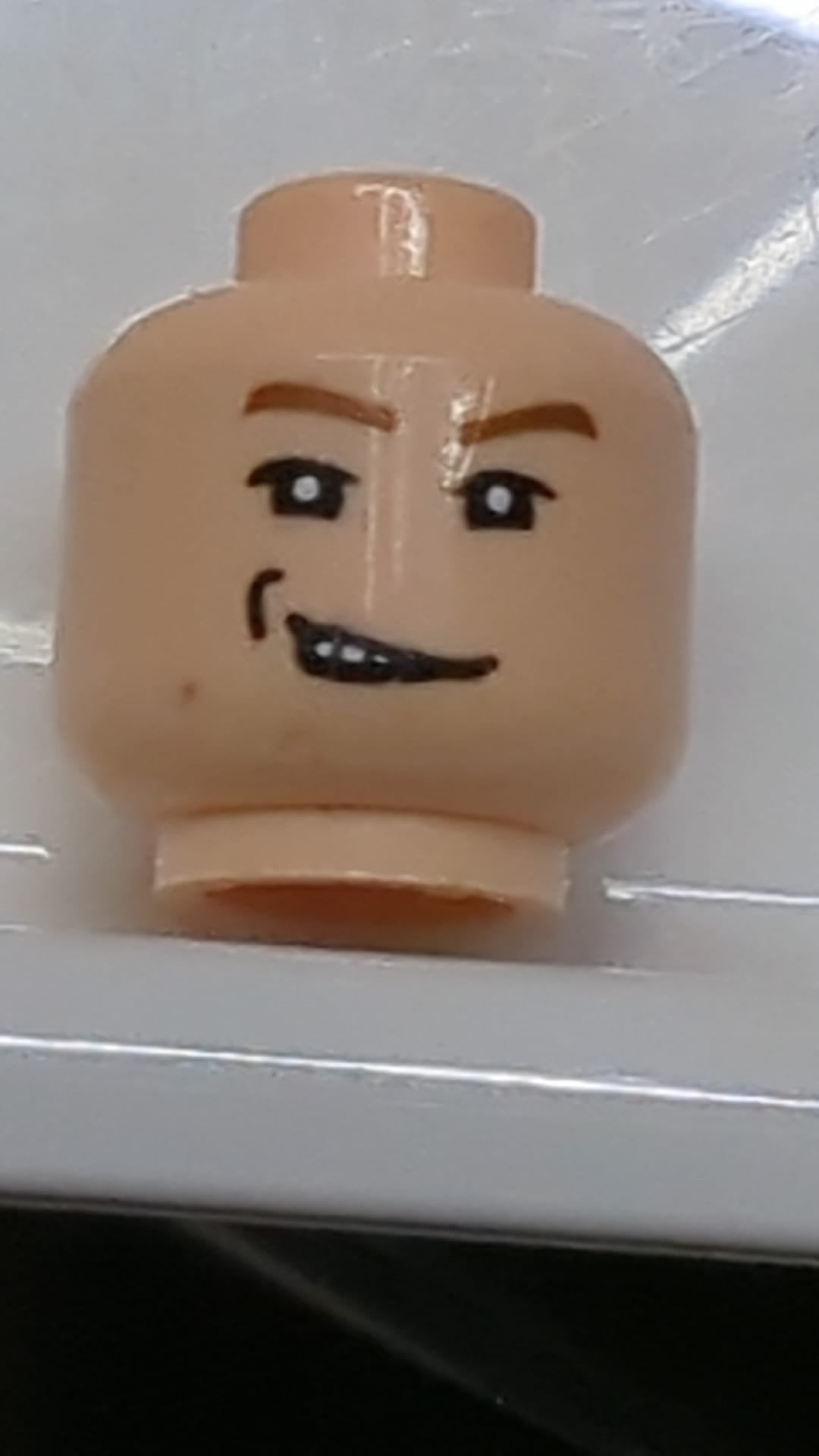 Minifigur, männlicher Kopf, braune Augenbrauen, weiße Pupillen, spöttischer Gesichtsausdruck, Grübchenmuster rechts hellnougat (fleischfarben)