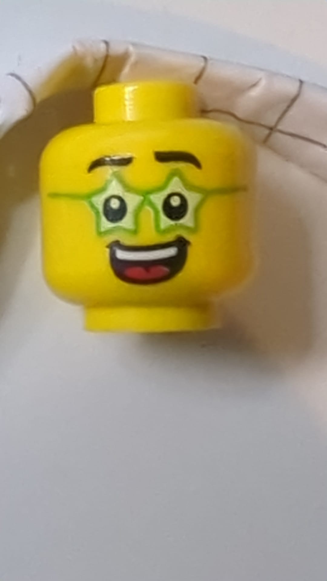 Minifigur, Kopf mit schwarzen Augenbrauen, leuchtend grüne, sternförmige Brille, breites, offenes Lächeln mit Zähnen und rotem Zungenmuster gelb