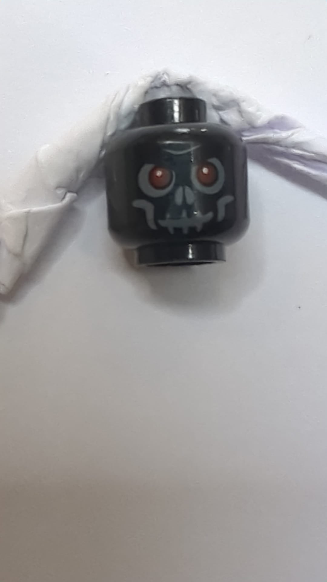 Minifigur, Schädelkopf mit roten Augen, dunkelblaugrauem Lidschatten, Wangenfalten, Mund und Nasenlöchern, zusammengezogener Stirn und grimmigem Grinsen schwarz
