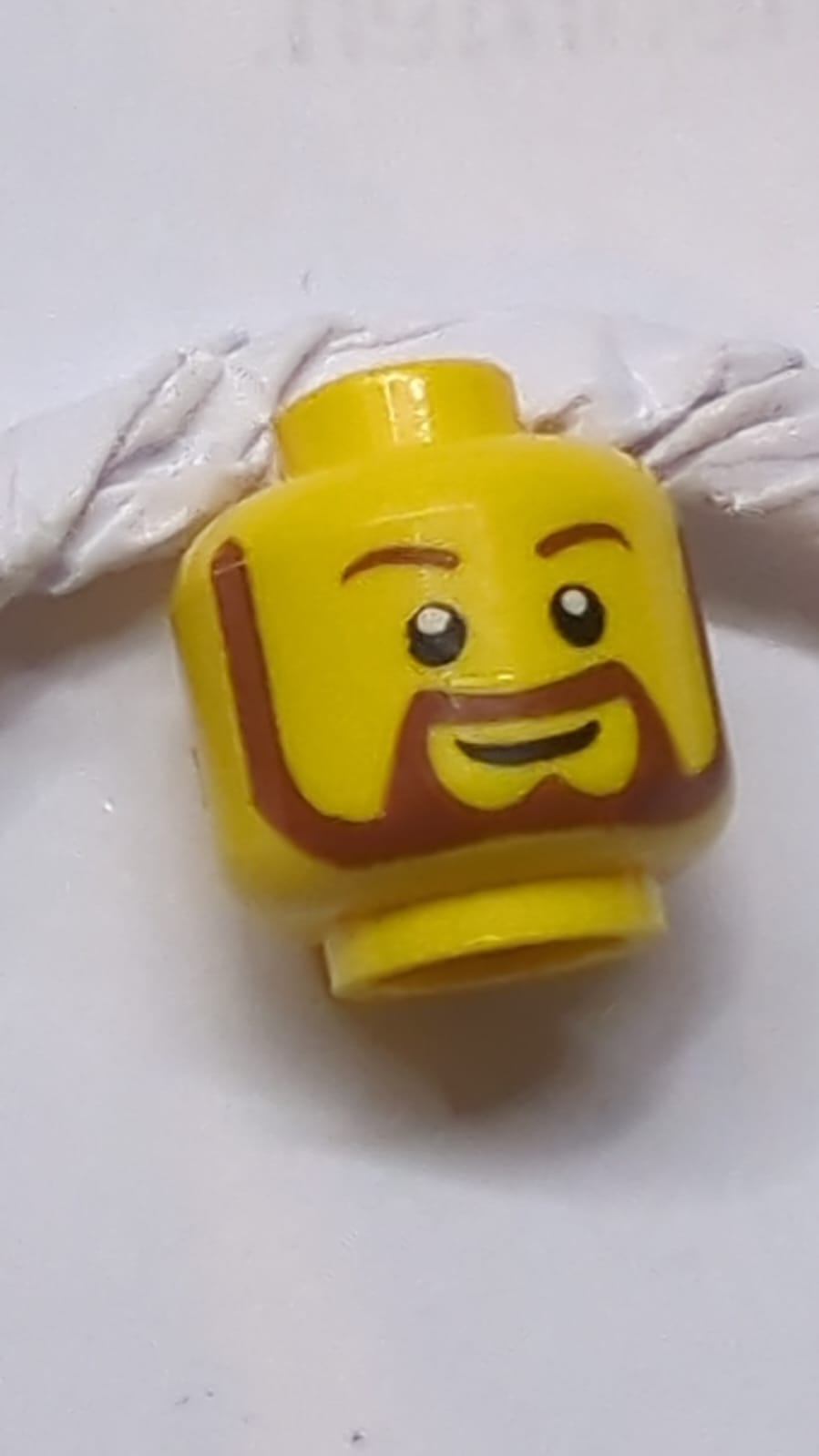 Kopf mit Bart rötlich-braun, rund mit weißen Pupillen und Grin-Muster gelb