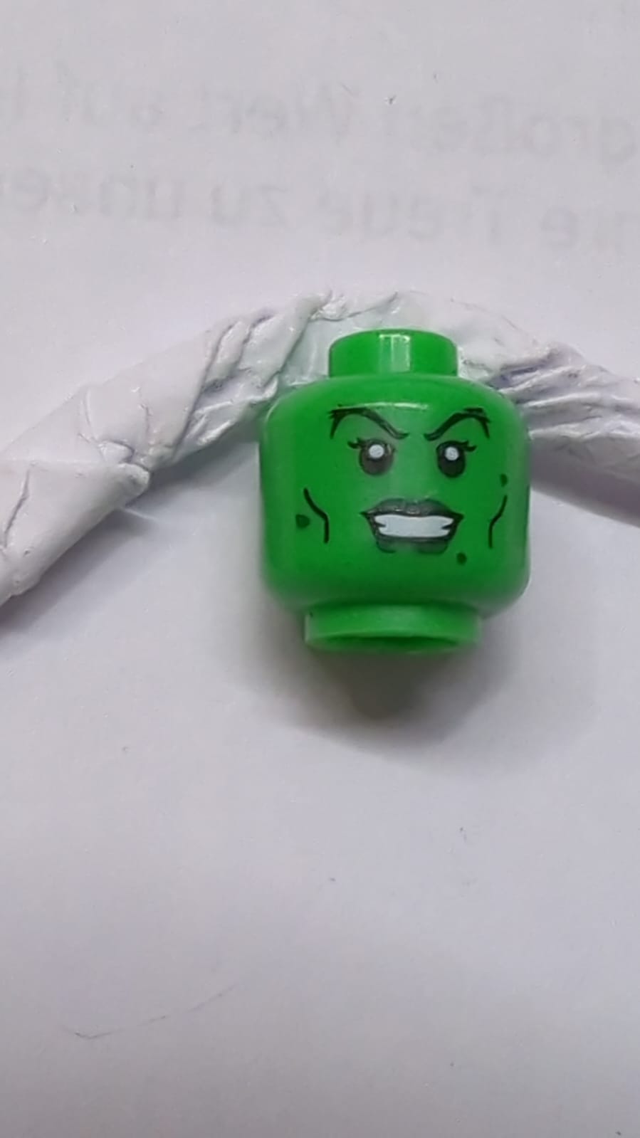 Kopf einer weiblichen Figur mit dunkelgrünen Lippen und Warzen, schwarzen Wangenlinien und Wimpernmuster mediumgrün