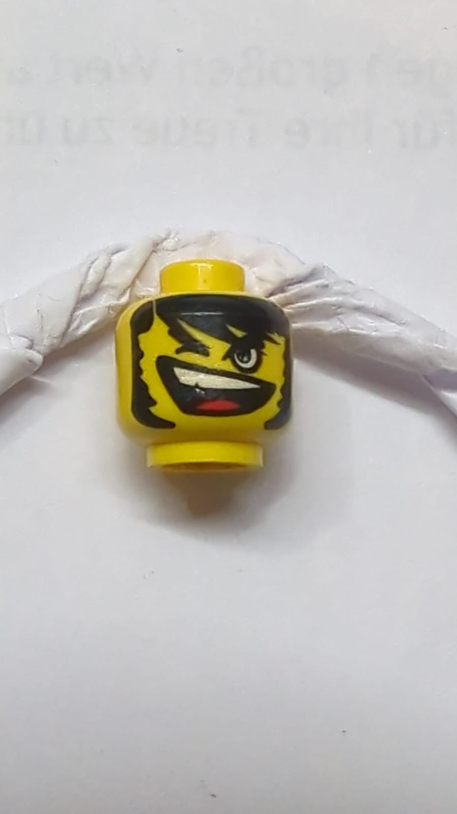 Kopf mit schwarzen buschigen Augenbrauen, Haaren und Koteletten, Augenzwinkern, schiefes offenes Mundlächeln mit oberen Zähnen und roter Zunge gelb