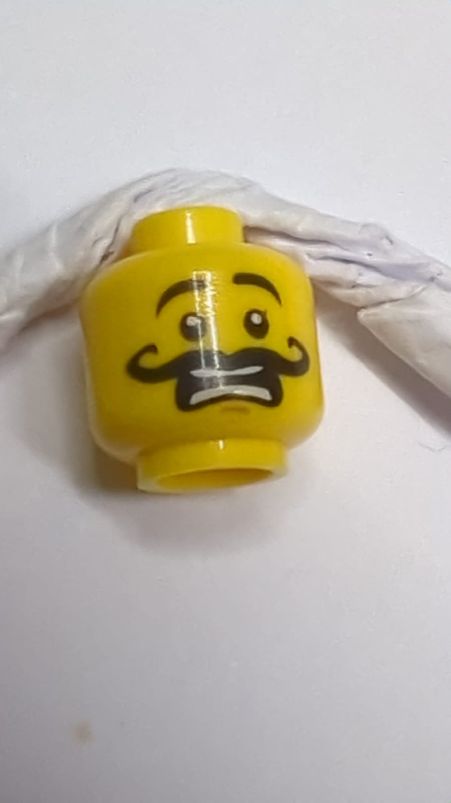Minifigur, Kopf mit schwarzen hochgezogenen Augenbrauen, lockiger langer Schnurrbart, mittlere Nougat-Kinngrübchen, erschrocken geöffneter Mund mit auseinanderstehenden Zähnen gelb