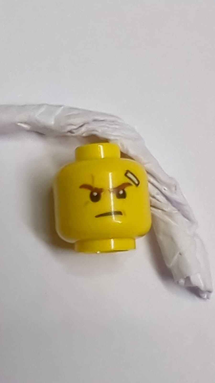 Minifigur, Kopf beidseitig Rötlich-braune Augenbrauen, mittlerer Nougatnarben, Verband, schiefer Grinsen mit Zähnen / Entschlossenes Muster (Kai) gelb