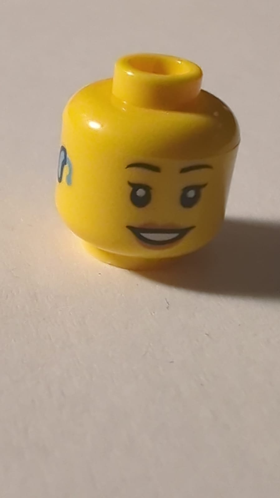 NEU Minifigur, weiblicher Kopf, schwarze dünne Augenbrauen, einzelne Wimpern, mittlere Nougatlippen, hellblaues Hörgerät rechts, offenes Lächeln mit Zahnstruktur gelb