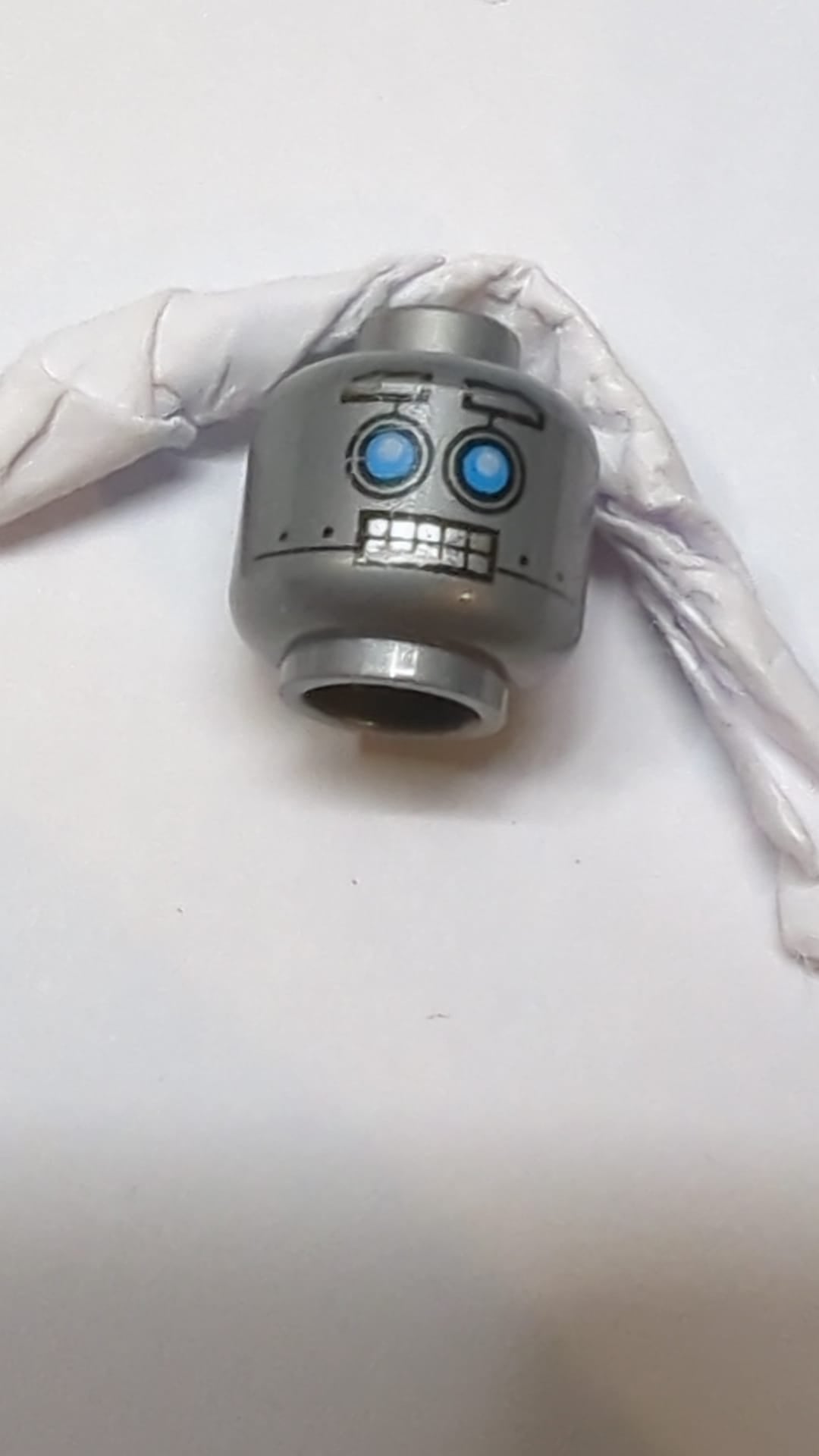 Minifigur, Alienkopf mit roboterhaften blauen Augen, hochgezogenen Augenbrauen, offenem Mund und zusammengebissenen silbernen Zähnen dunkles Pearlsilber