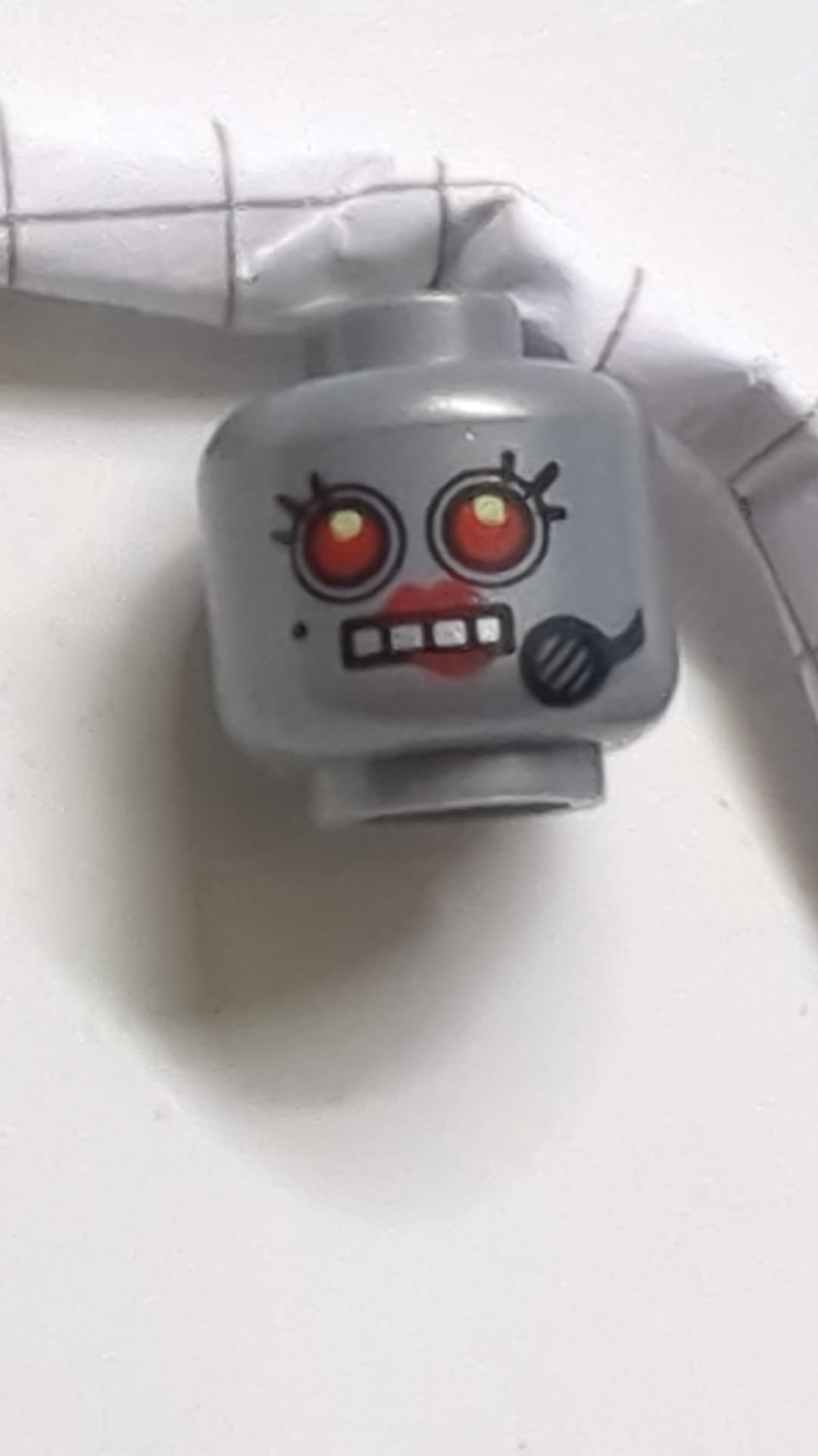 Minifigur, Kopf eines weiblichen Alien-Roboters mit schwarzem Schönheitsfleck und Mikrofon, roten Augen und Lippen sowie offenem Mund mit silbernem Zahnmuster dunkles Pearlsilber