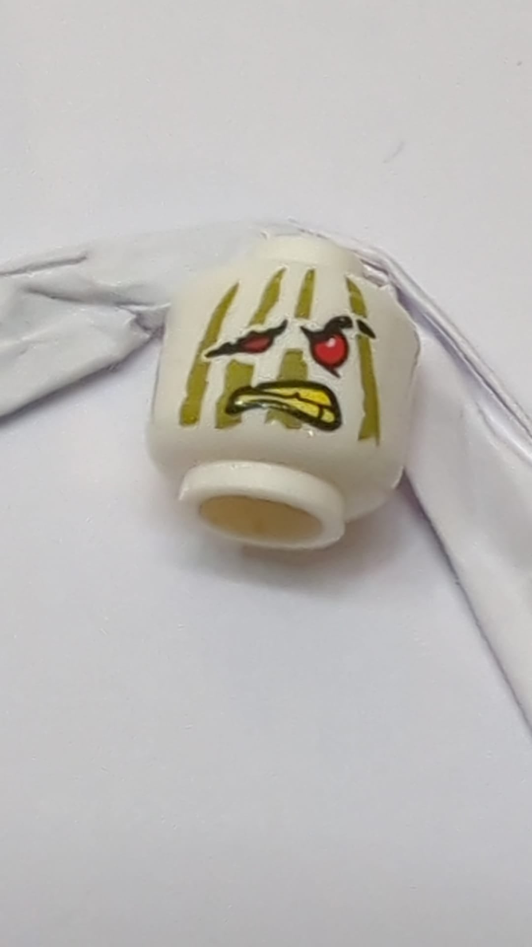 Minifigur, Kopf: Alien Ninjago, rote Augen, hängendes rechtes Auge und Mund, olivgrüne Streifen, gelbes Zahnmuster weiß