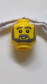 Minifigur, Kopf dunkelblaugrau, dichte Augenbrauen, kantiger Bart und dünne, spitze Koteletten, offenes Lächeln mit weißem Zahnmuster gelb