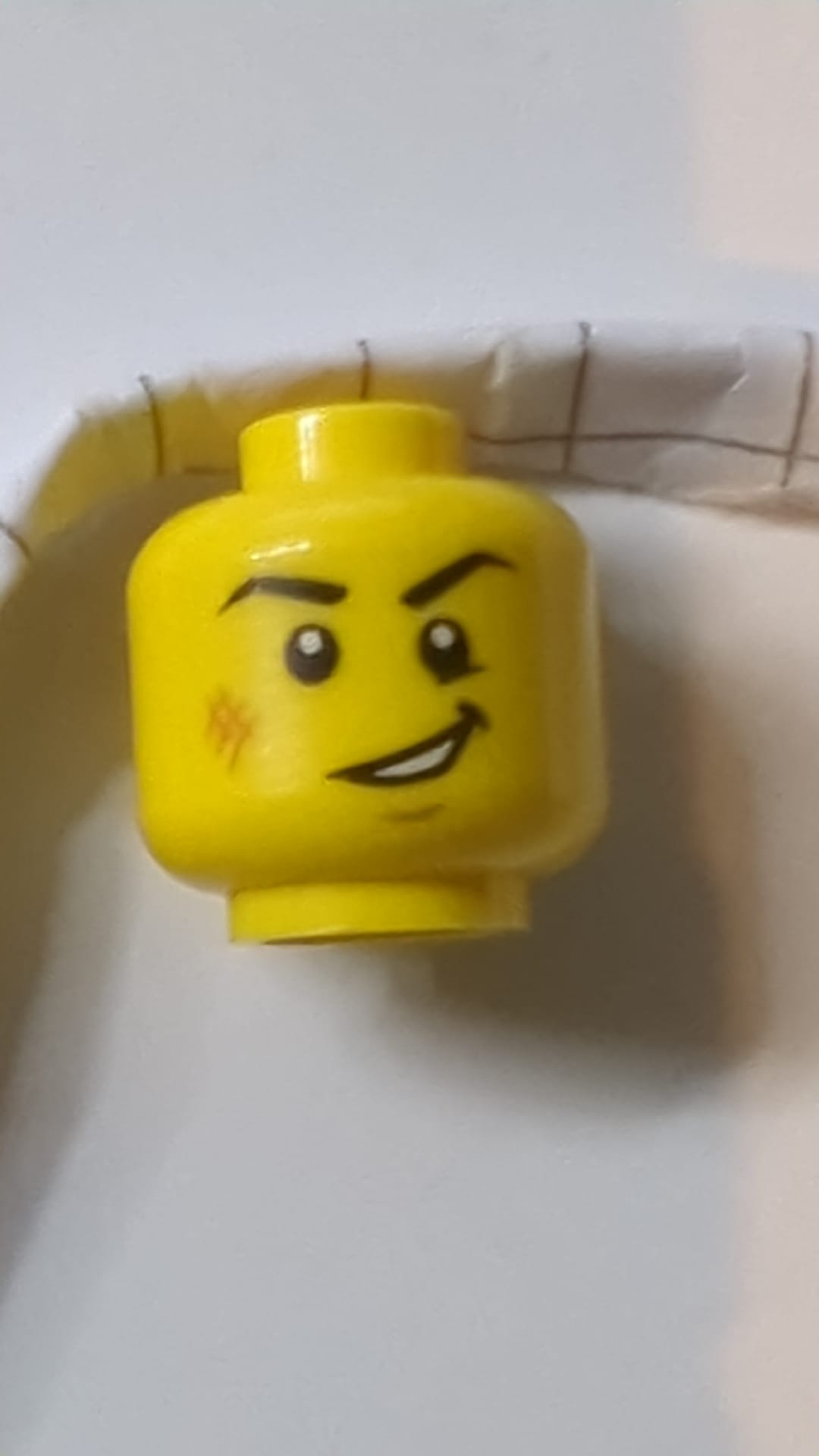 Minifigur, Kopf mit schwarzen Augenbrauen, rechtwinklig, mittelgroßer nougatfarbener Kratzer und Grübchen am Kinn, schiefer, offener Mund mit sichtbarem Zahnmuster gelb