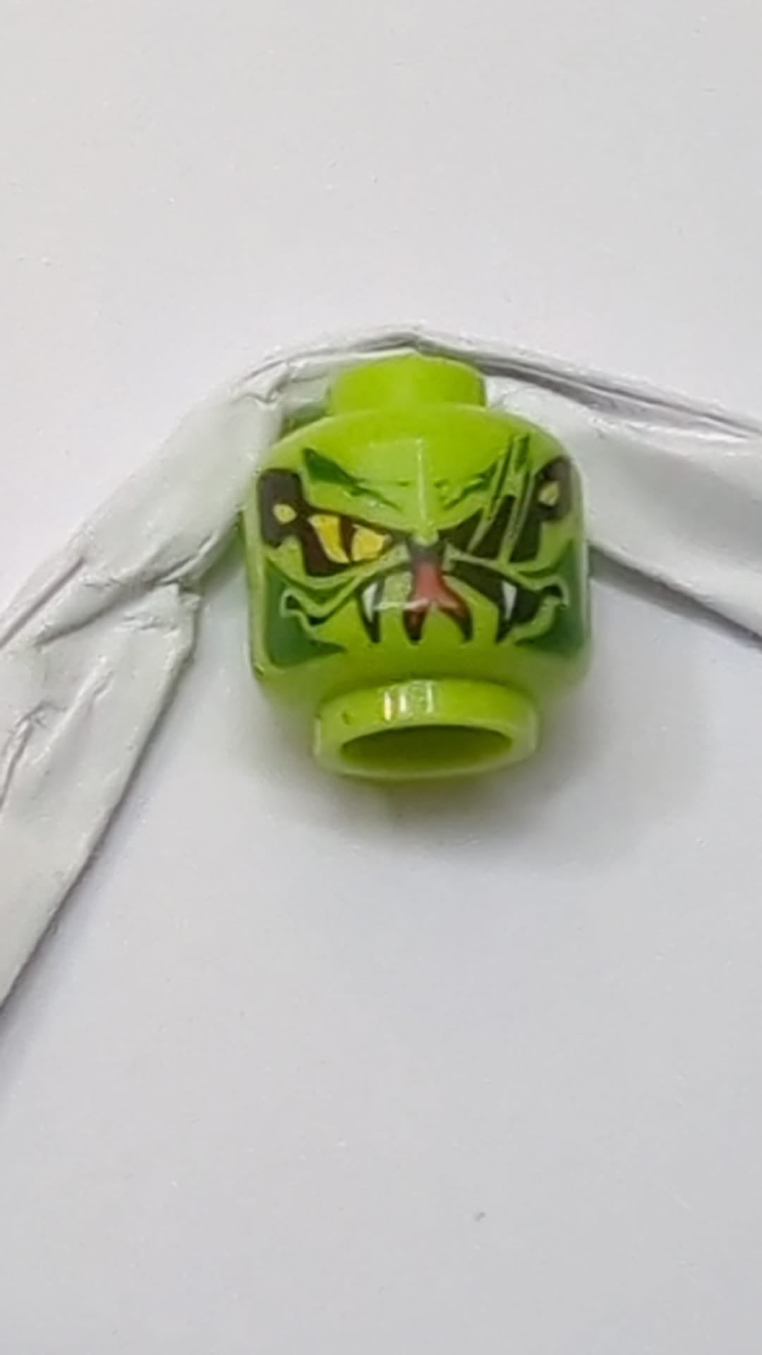 Minifigur, Kopf einer außerirdischen Schlange mit großen gelben Augen mit schwarzen Schnittnarben, dunkelgrünen Markierungen, Maul mit weißen Reißzähnen und rotem, gespaltenem Zungenmuster lindgrün