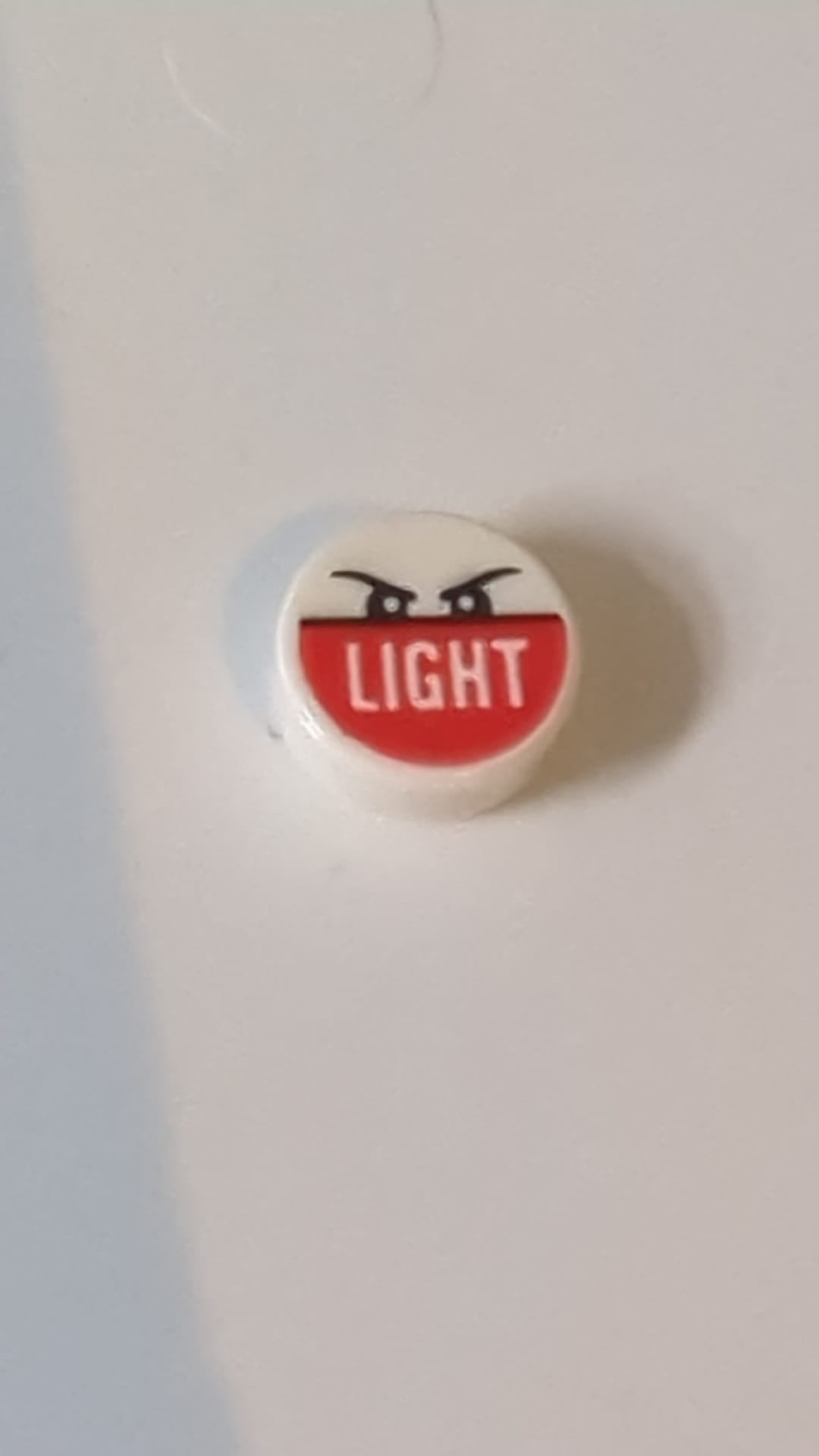 1x1 Fliese rund mit schwarzen, wütend wirkenden Augenbrauen und Augen, Schriftzug „LIGHT“ auf rotem Hintergrundmuster weiß