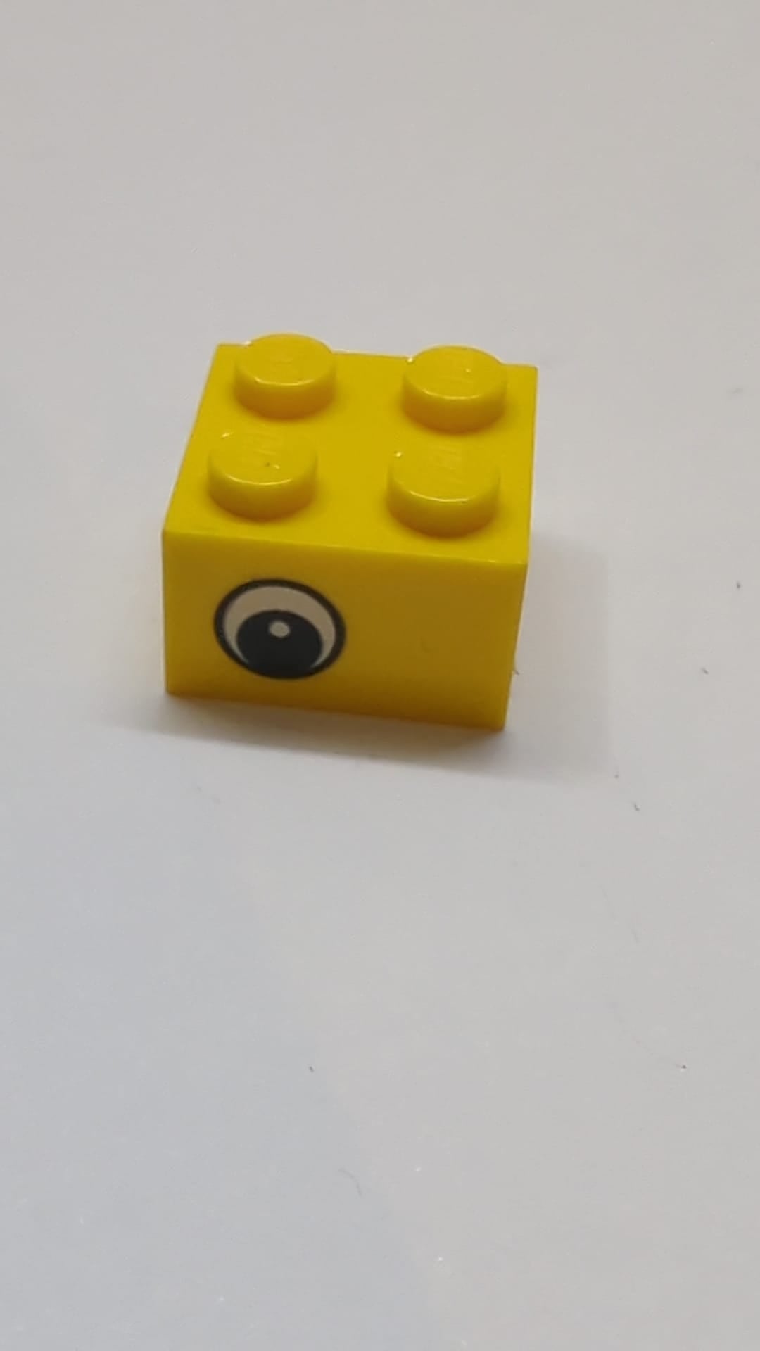 2x2 Stein mit versetztem schwarzem und weißem Auge und Punktmuster in der Pupille auf gegenüberliegenden Seiten gelb