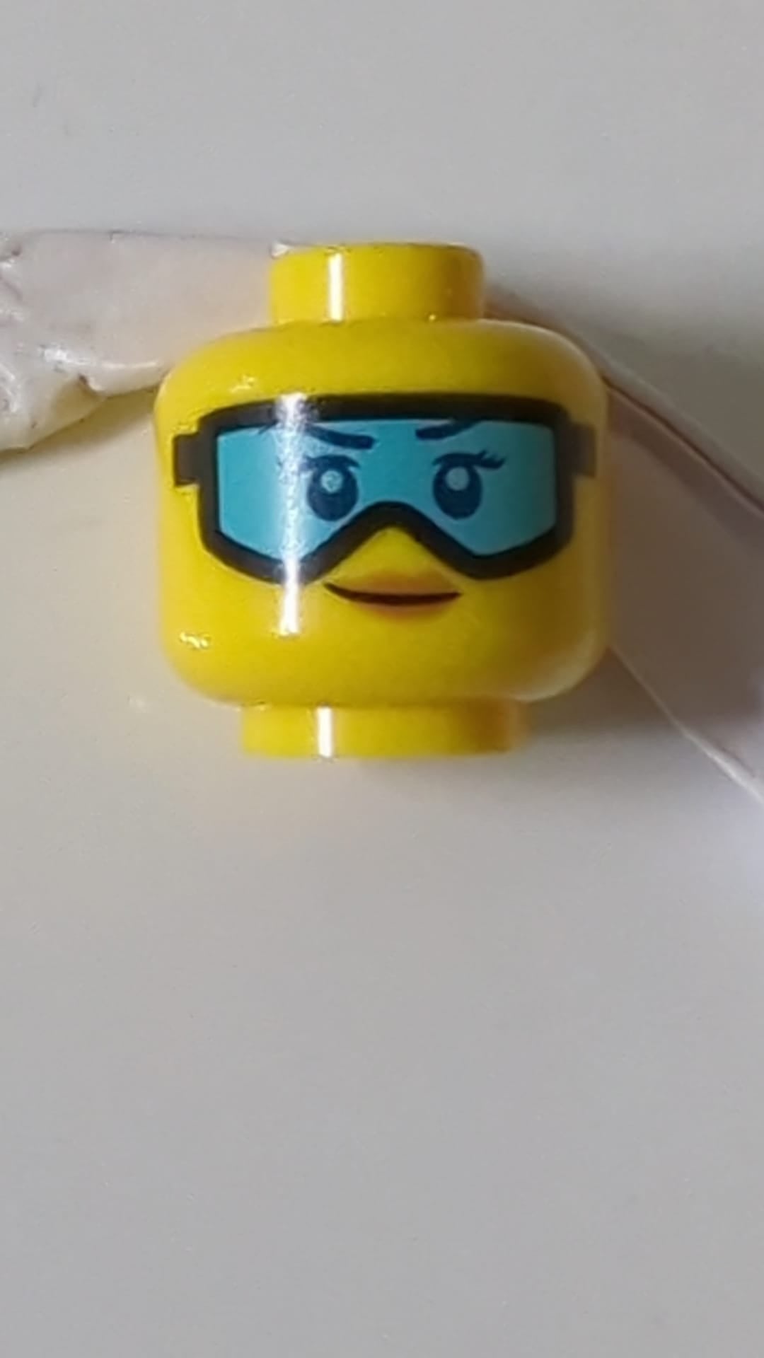 Minifigur, weiblicher Kopf, dunkelblaue Augenbrauen, Wimpern und Augen, schwarze Skibrille mit mittelblauen Gläsern, nougatfarbene Lippen, Grinsen gelb