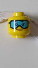 Minifigur, weiblicher Kopf, dunkelblaue Augenbrauen, Wimpern und Augen, schwarze Skibrille mit mittelblauen Gläsern, nougatfarbene Lippen, Grinsen gelb