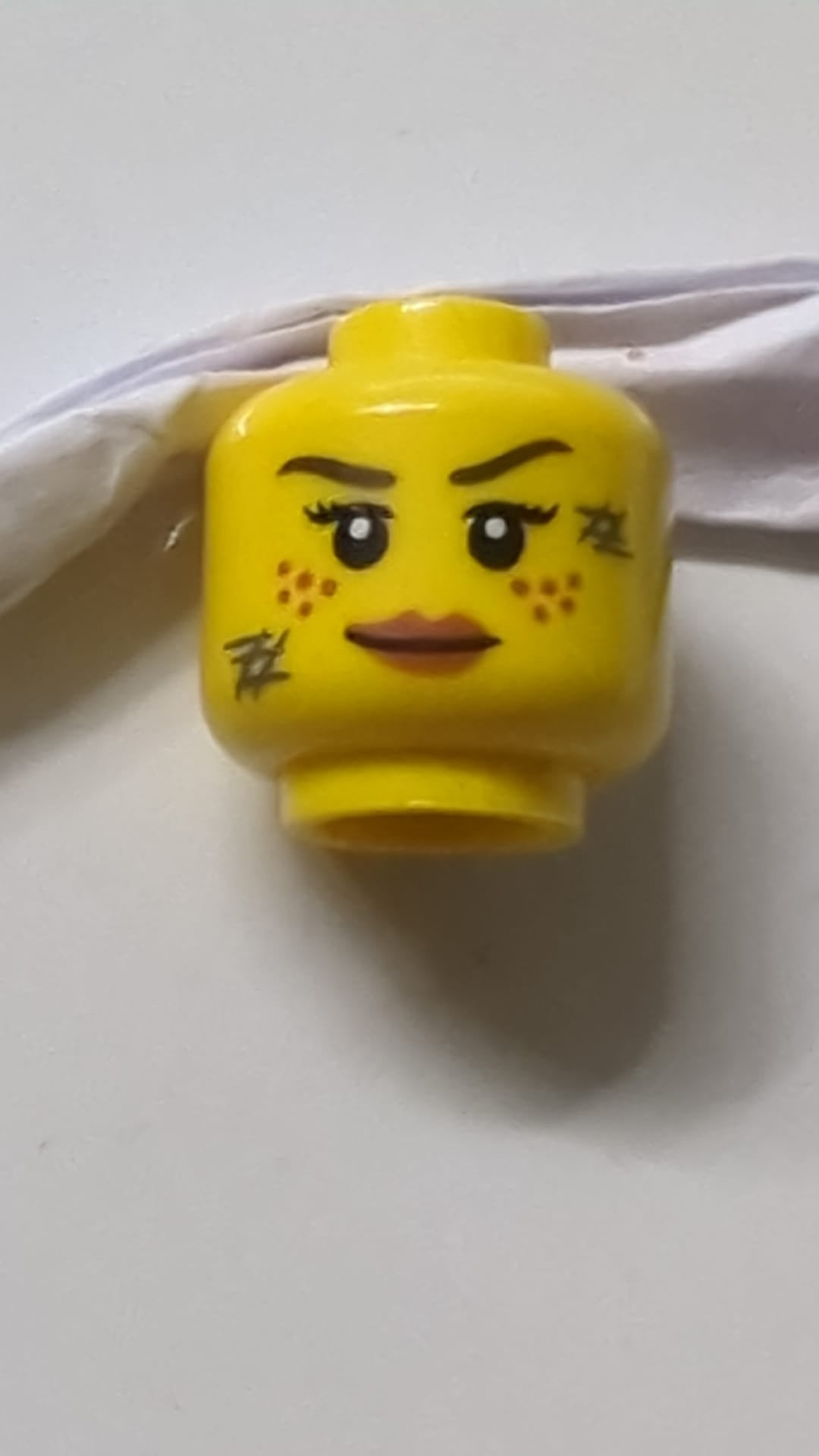 Minifigur, Kopf, weiblich, dunkelbraune Augenbrauen, dunkelorange Sommersprossen, Wimpern, dunkelblaugraue Kratzer, dunkelorange Lippenmuster gelb