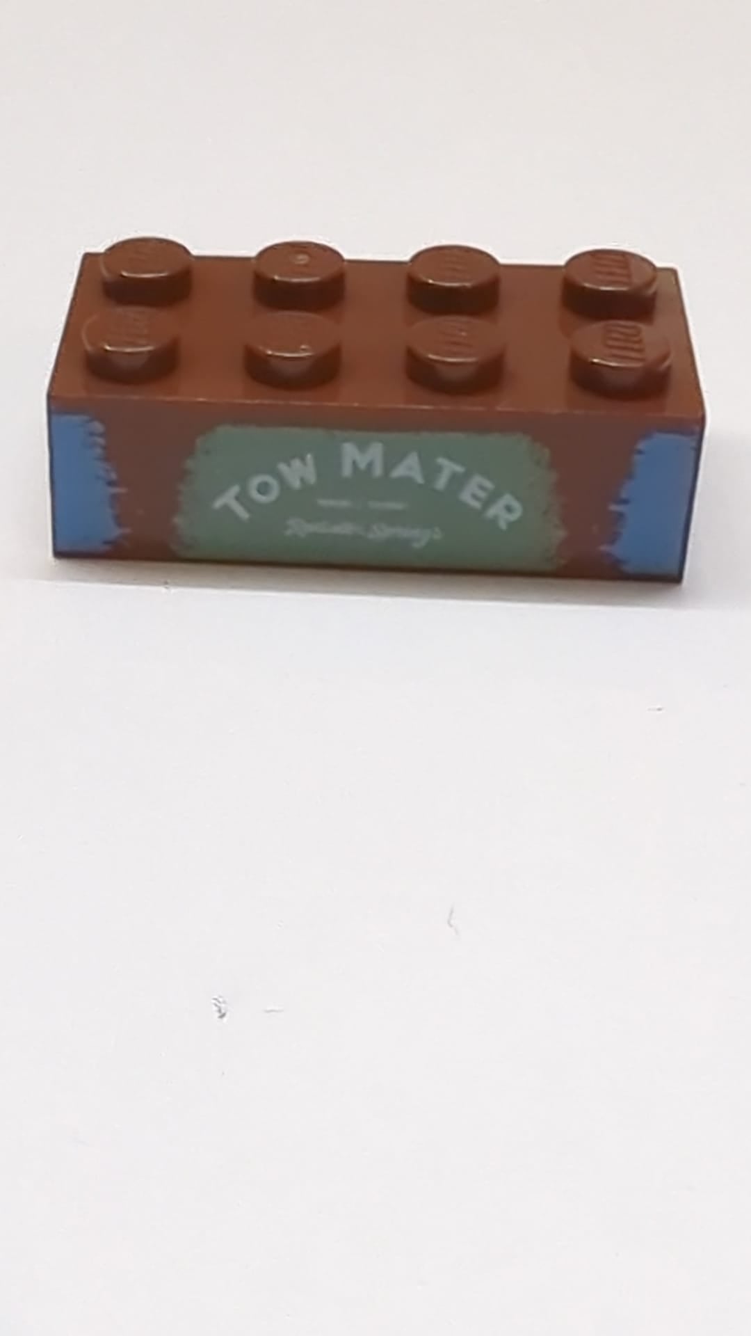 2x4 Stein mit der Aufschrift „TOW MATER“ auf sandgrünem Hintergrundmuster neubraun